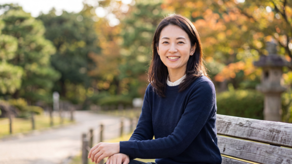 Smiling Japanese woman sitting on a park bench in autumn trees